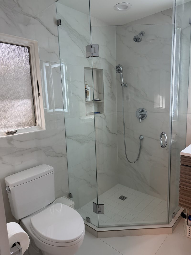 Marble shower enclosed in glass with chrome fixtures and built-in niche