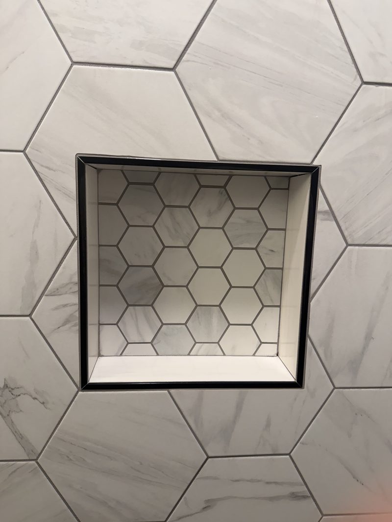 Black-trimmed niche with hexagon mosaic against large-format marble