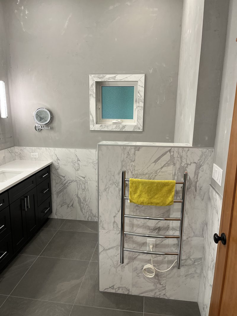 Custom black double-vanity bathroom with marble walls and backlit mirrors